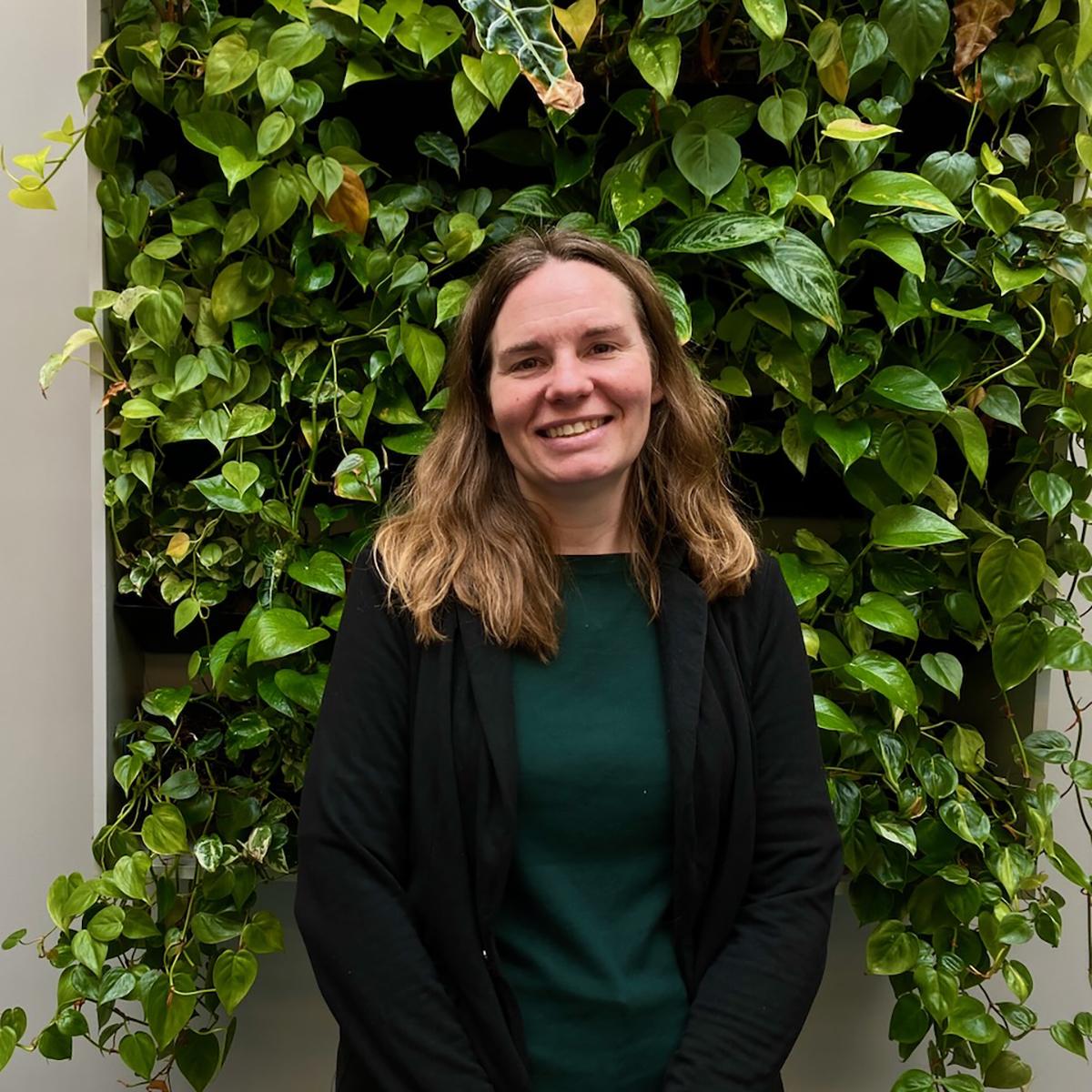 Portrait of Chrissy Daeschner smiling against a green plant wall